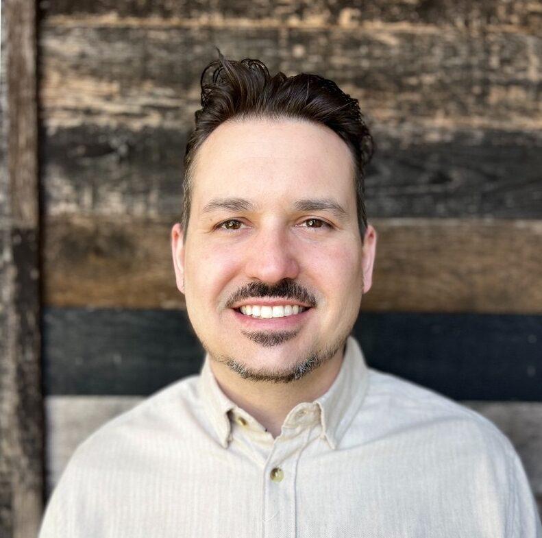 Nick Friar, sr. Operations manager at Duck Donuts smiling in front of wall